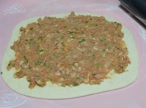 把调好的肉馅取一部分铺在面饼上，尽量摊的均匀一些；