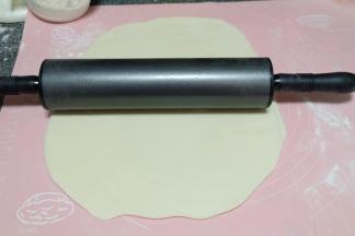 我是先揉的白色面团，所以先把白色面团取过来，撒上一些干面粉防粘，用擀面杖擀开成一个大的饼状；然后转移到旁边备用；