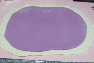 把两种颜色的面饼叠在一起，白色的在下面，紫色的在上面；白色的因为面粉比较多，擀的略大了一些；