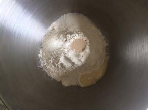面桶内倒入高筋面粉，中间挖一小孔倒入活性干酵母，盐和糖对角线放置，炼乳倒入，加入清水，启动厨师机和面