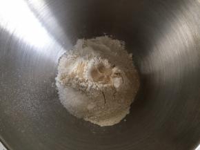 披萨饼底的制作：全麦高筋面粉倒入厨师机内，挖一小孔倒入活性干酵母，糖和盐对角线放置，倒入清水，开启中速搅拌