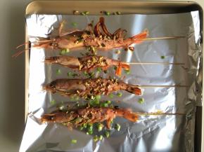 把串好的虾放入铺了锡箔纸的烤盘内，把料汁均匀刷在虾上，再撒上适量葱段