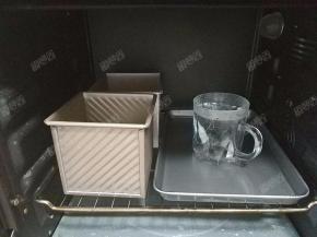 将吐司盒放入烤箱中，再放入一杯温水进行发酵