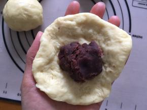 拿出一个面团，压扁，将红豆沙放在中间，包住，