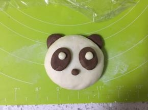 另取两个可可小面团，搓成椭圆形，按扁，沾一点水沾在熊猫的脸上，白面团粘在眼袋上，再取一点点可可面团作为鼻子