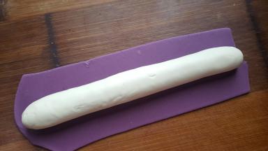 9．把红色面团擀成面皮，白色面团揉圆滚长，红色面皮包好白色面团，收口处捏紧。