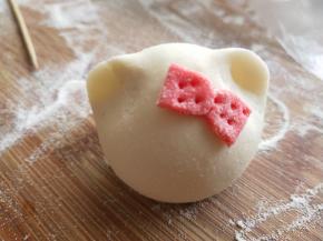 面团上抹少许水。把蝴蝶结粘在耳朵前方合适的位置，用牙签戳几下装饰同时可以更好的固定蝴蝶结