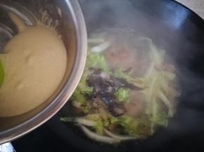 水开后，放黑木耳，开始下面疙瘩，就这么倾斜，沿着碗边用刮刀把面糊切下来，往煮沸的地方切，这样疙瘩会迅速成型，不会煮成糊糊