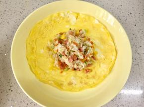 把适量的炒饭舀入蛋皮中间，边缘捏褶把饭包起，收口用焯过的玉米叶撕成的细条扎起来。