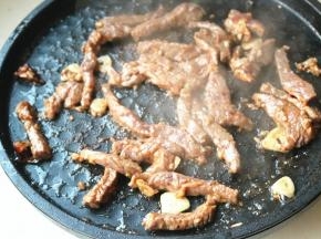 电饼铛开下盘，下入色拉油烧热并爆香蒜片辣椒。下入腌好的牛肉条翻炒至变色。