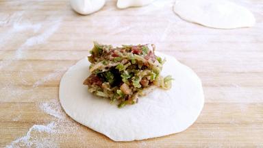 小剂子按扁，擀成中间略厚，四周薄的包子皮，中间放馅。