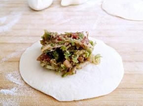 小剂子按扁，擀成中间略厚，四周薄的包子皮，中间放馅。