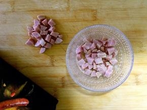 取3根纯肉香肠切条再切丁。分出两部分，多的放在面团中，少的放在面包生胚表面。