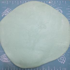 案板上撒一些糖粉，手上抹白油，量好蛋糕的大小，将主体颜色的翻糖膏擀成片，注意不要过于薄