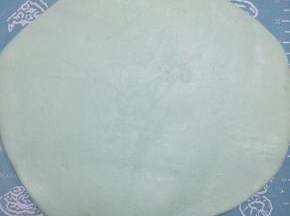 案板上撒一些糖粉，手上抹白油，量好蛋糕的大小，将主体颜色的翻糖膏擀成片，注意不要过于薄