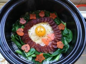快速把青菜、腊肠、胡萝卜摆成自己喜欢的造型，打入一个鸡蛋，洒上一点黑芝麻，从边缘倒入少量油，盖上锅盖，用最小火煮三分钟，然后关火继续焖15分钟。