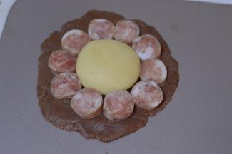 取一份可可面团，揉圆后压扁，用擀面杖轻轻杆开，不要太薄，不然烤好后不好拿起来。然后再取一份白年团揉圆，放在上面，再依次围上香肠，形成一个狮子的模样。