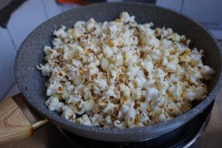 很快就看到玉米粒在锅中跳舞变形，噼哩啪啦的声音非常好听。（摇晃一下平底锅）。看！小小一包就能爆出一大锅了