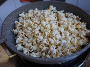 很快就看到玉米粒在锅中跳舞变形，噼哩啪啦的声音非常好听。（摇晃一下平底锅）。看！小小一包就能爆出一大锅了