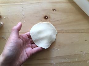 左手拿着面皮，右手用擀面杖擀，擀成中间稍微厚一点，边沿薄的饺子皮