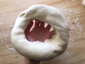 松弛好的面团取出，在案板上撒适量面粉，把面团中间抠个洞，从孔中间往外圈把孔撑大