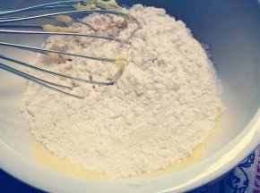 将黄油蛋液分装在两个盆中 倒入一半低筋粉搅拌