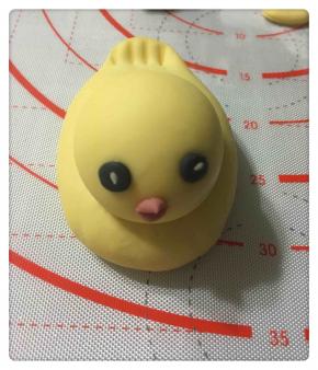 用竹碳粉、红曲粉少许和白面团调成黑色和红色，竹碳粉调成的黑面团做眼睛，红曲粉面团做嘴巴。眼睛搓成圆形，上面放一颗白芝麻。嘴巴切成菱形，同样需沾少许水以便黏牢，如图所示。