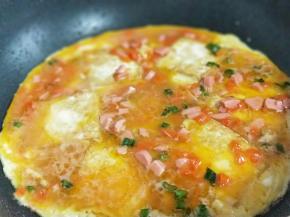 倒入调好的蛋液，撒上熟黑芝麻，煎至蛋液凝固即可出锅。