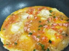 倒入调好的蛋液，撒上熟黑芝麻，煎至蛋液凝固即可出锅。