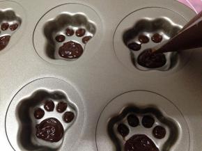 将巧克力面糊的裱花袋剪开一个小口，均匀的将面糊挤到猫爪蛋糕模具内的猫爪肉垫内