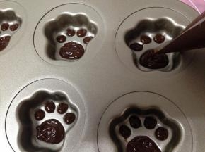 将巧克力面糊的裱花袋剪开一个小口，均匀的将面糊挤到猫爪蛋糕模具内的猫爪肉垫内
