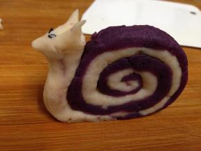 另取剩下的山药泥捏成头部，用两粒黑芝麻做眼睛，如图安装到蜗牛壳上，整形