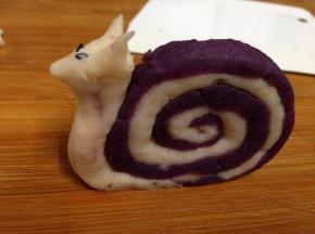 另取剩下的山药泥捏成头部，用两粒黑芝麻做眼睛，如图安装到蜗牛壳上，整形