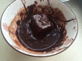 100克巧克力在35克牛奶里溶化。把蛋糕块放入裹上巧克力酱