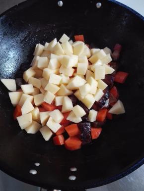 放入葱蒜、胡萝卜丁翻炒，几分钟后放入土豆丁炒匀；不用放盐调味，腊肉比较咸