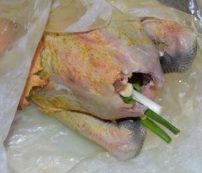 2，腌制好的鸡，在肚子里塞入两根葱，同时也把鸡腿塞进肚子里。其中一张砂纸涂上食用油，包裹着整鸡，再用另一张砂纸把鸡完全包裹住。
