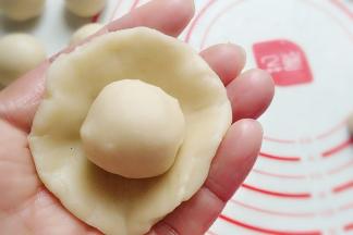 取一份油皮按扁成圆形，再放入一份油酥在中间，像包小笼包一样捏起包圆；