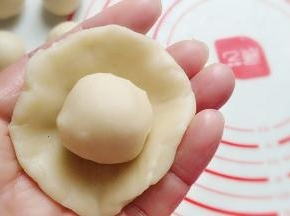 取一份油皮按扁成圆形，再放入一份油酥在中间，像包小笼包一样捏起包圆；