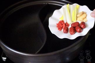 在鸳鸯锅的一边、加入葱段、姜片、枸杞和红枣