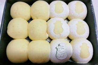 将发酵好的面包胚取出，找一个雪人饼干模具放在面包胚上，挨个小心地筛上一层高粉，然后移开雪人模具；