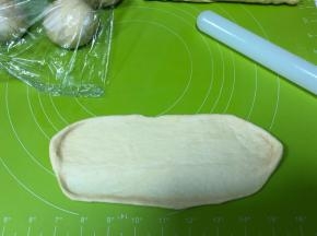 松弛好的面团按扁，擀成椭圆，一边长边刻意擀薄一点便于粘合