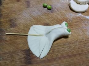 前段中间往里收，捏成两个小孔当作金鱼的眼睛，分别在小孔里面放两粒小豌豆，尾巴处先用牙签压出花纹印记，然后如图在尾巴处对称切两刀，分割出鱼鳍部分