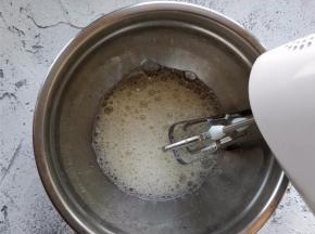 用电动打蛋器朝一个方向打发蛋清，形成鱼眼泡时，加入一半量的细砂糖打发。