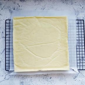 用手提起金盘内油纸边缘，将蛋糕体倒扣在晾网上，撕掉底部的油纸晾凉。