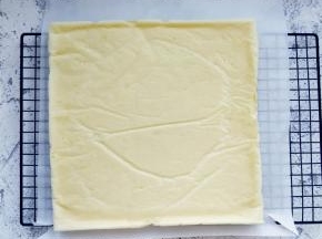 用手提起金盘内油纸边缘，将蛋糕体倒扣在晾网上，撕掉底部的油纸晾凉。