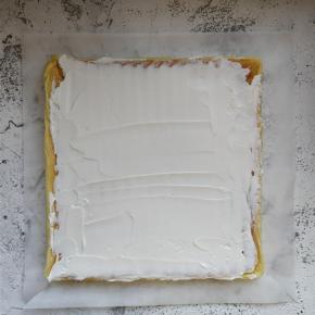 用刮刀将适量奶油涂抹在摊平的蛋糕体上，在起始卷的一侧，奶油可稍厚些。