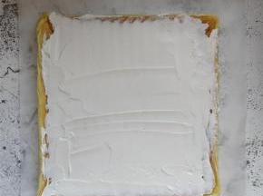 用刮刀将适量奶油涂抹在摊平的蛋糕体上，在起始卷的一侧，奶油可稍厚些。