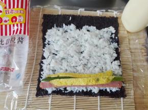 在紫菜上铺上米饭，边缘留一点不要放米饭，尽力铺的厚薄一致，放上黄瓜条、火腿肠的条、蛋皮条（这些都需要事先切好）；