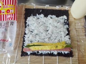 在紫菜上铺上米饭，边缘留一点不要放米饭，尽力铺的厚薄一致，放上黄瓜条、火腿肠的条、蛋皮条（这些都需要事先切好）；