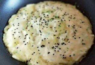 平底不沾锅中加入少许食用油，盛2勺面糊，用铲子摊平即可。再撒上熟黑芝麻。中小火煎至两面微黄。